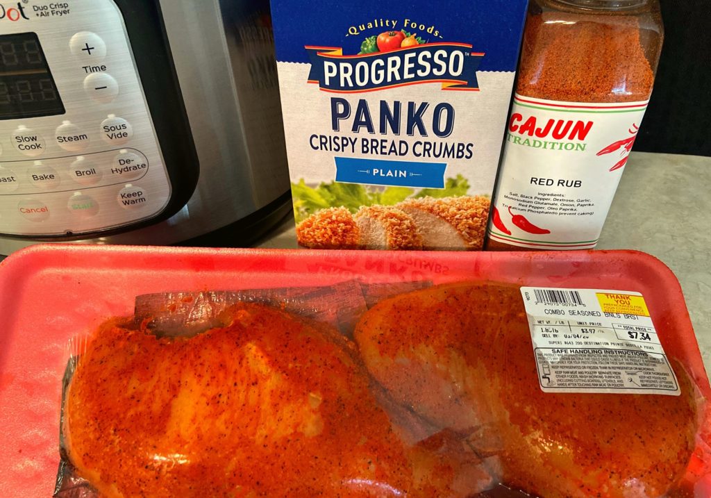A instant pot duo crisp plus air fryer, box of panko crispy bread crumbs, cajun red rub seasoning, and two chicken breasts sitting on a kitchen counter.