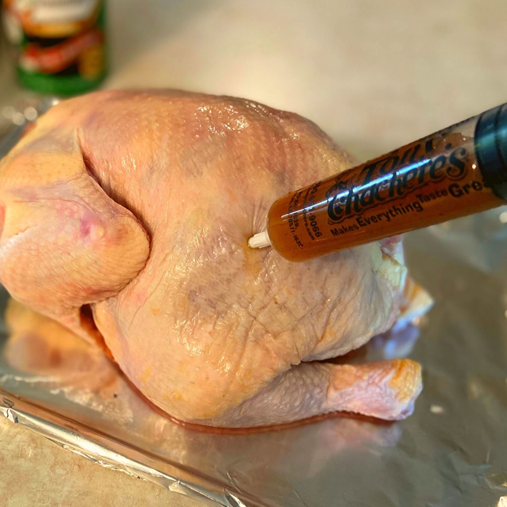 A raw chicken on a kitchen counter being injected with tony chachere's butter marinade.