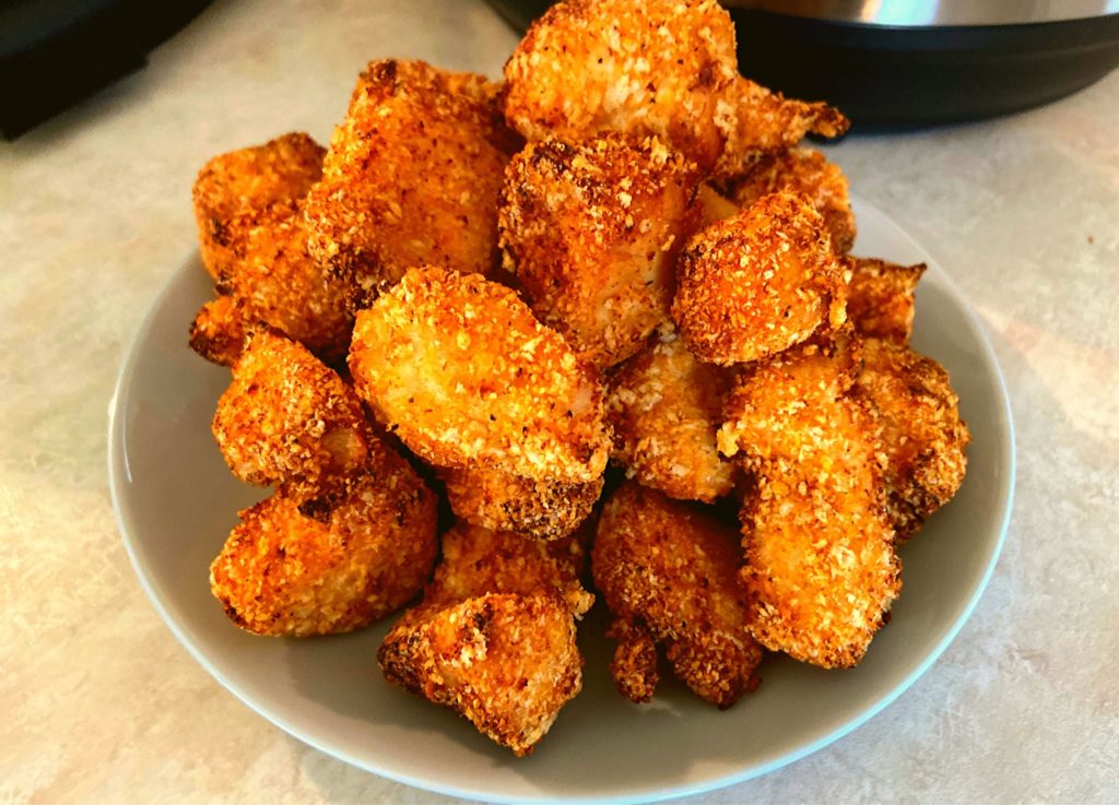 A round grey plate topped with air fried boneless chicken bites sitting in front of an Instant Pot Duo Crisp plus air fryer.