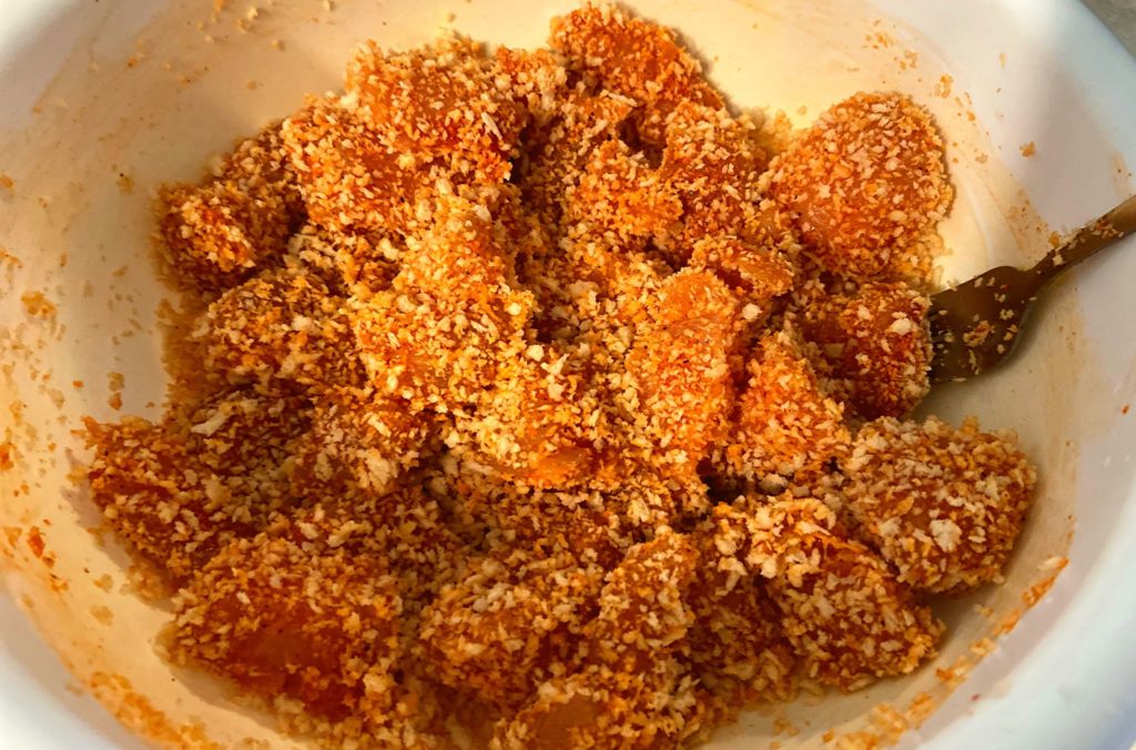 A white bowl filled with raw boneless chicken bites covered in panko bread crumbs and seasoning.