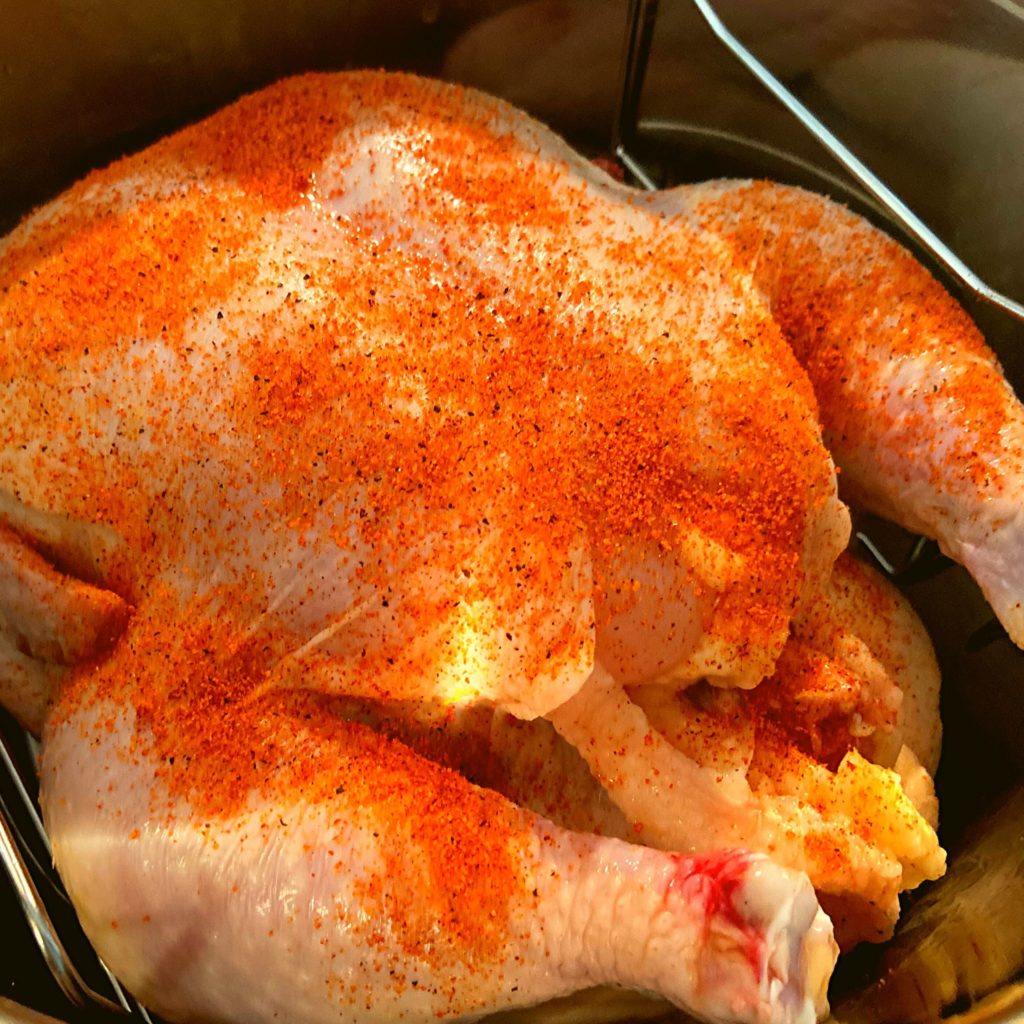 A whole raw chicken covered with seasoning in and Instant Pot Duo Crisp on a trivet.