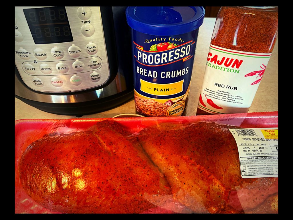 An Instant Pot Duo Crisp sitting on a kitchen counter top with two raw chicken breasts, cajun seasoning, and breadcrumbs.