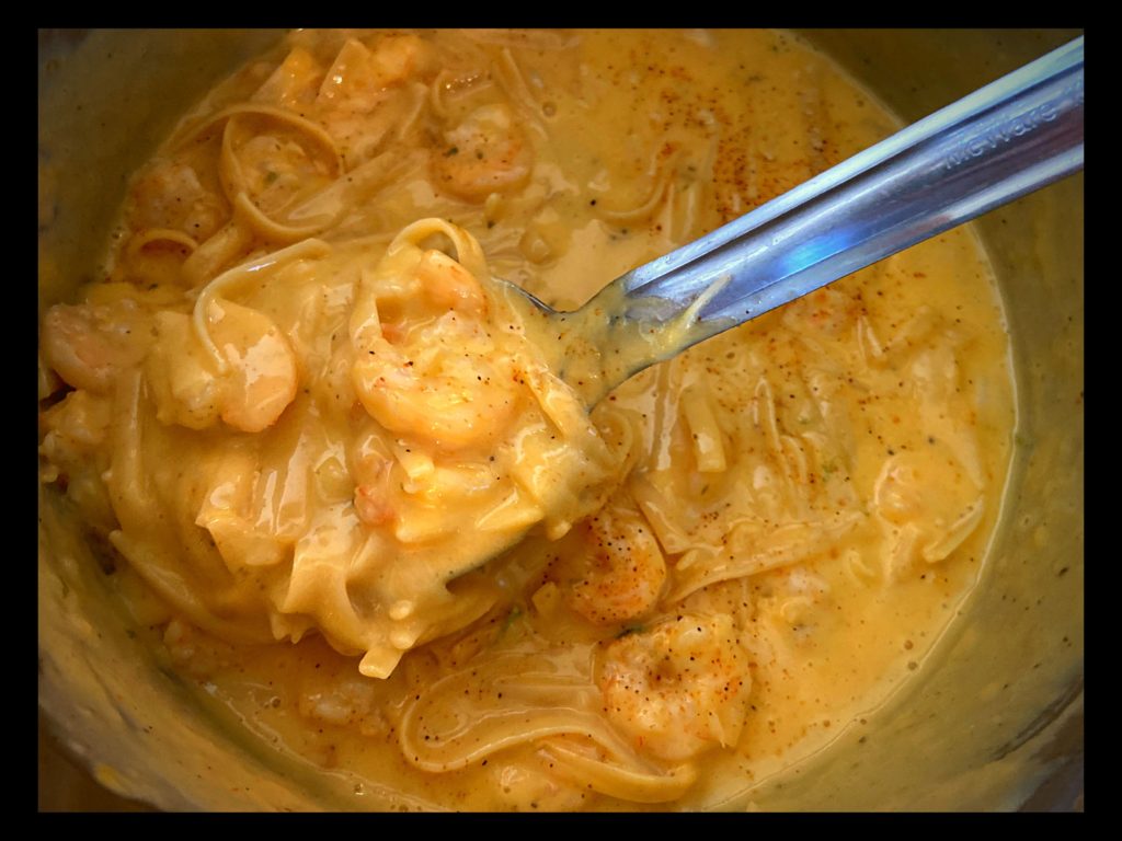 An instant pot filled with cajun shrimp fettuccine with velveeta cheese and a large spoon.