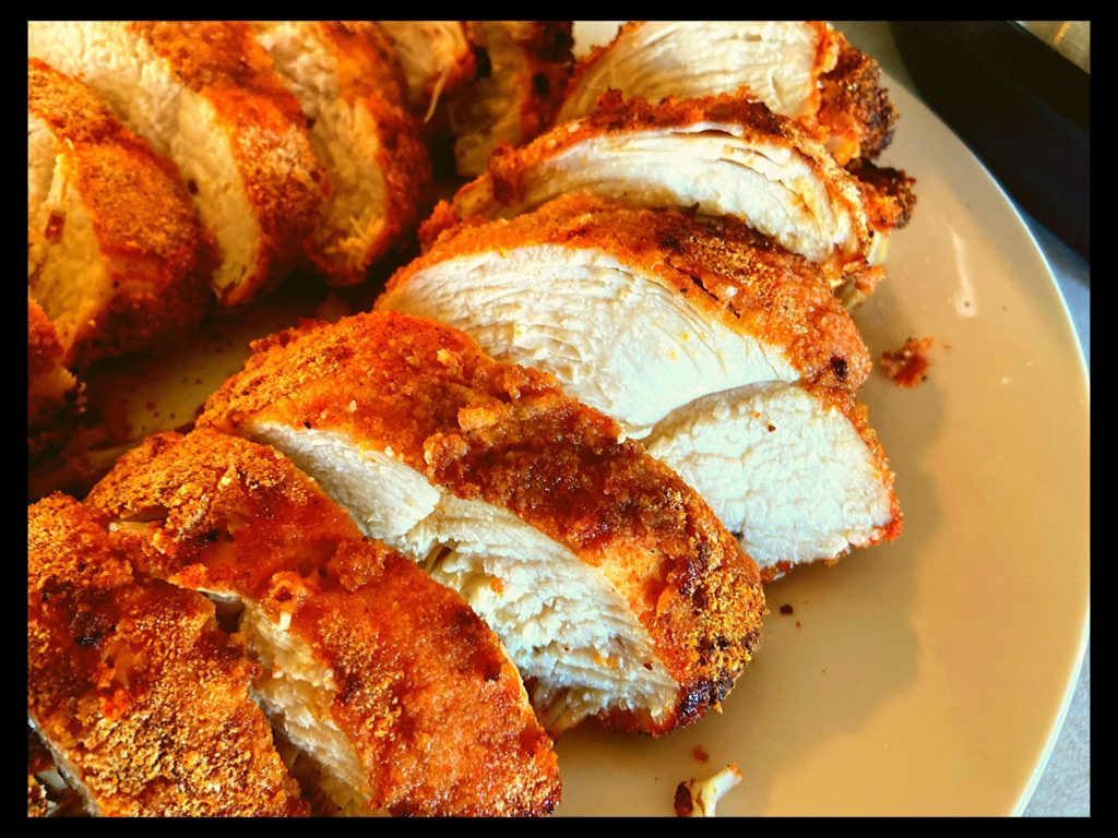 Crispy air fried breaded chicken breasts sliced into 1 inch sections on a white plate.