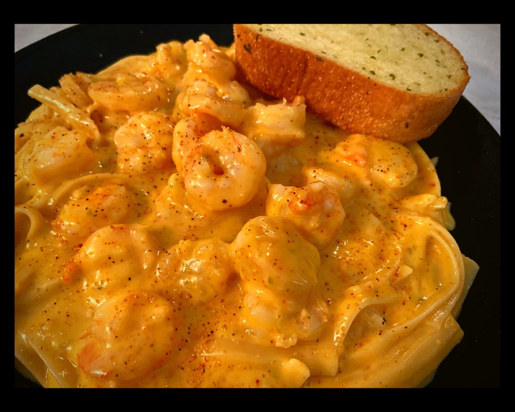 A black plate filled with Instant Pot Cajun Shrimp Fettuccine with Velveeta Cheese and a garlic bread.