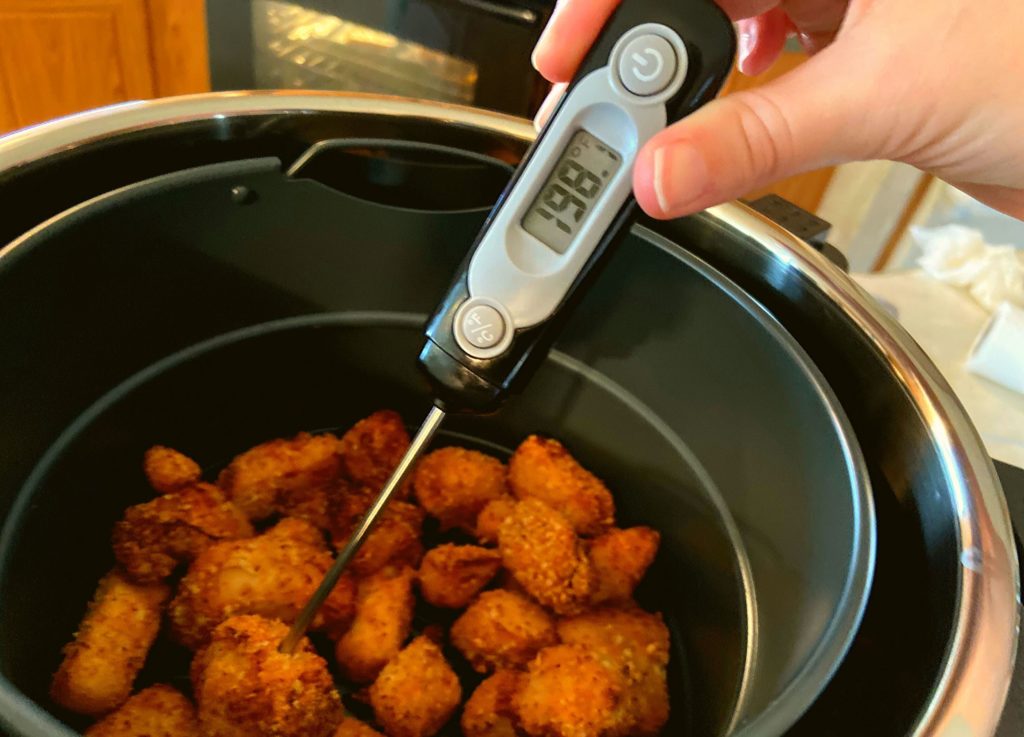 Instant Pot Duo Crisp Boneless chicken bites in the Instant Pot air fryer basket with a meat thermometer sticking out reading 198 degrees internal temperature.