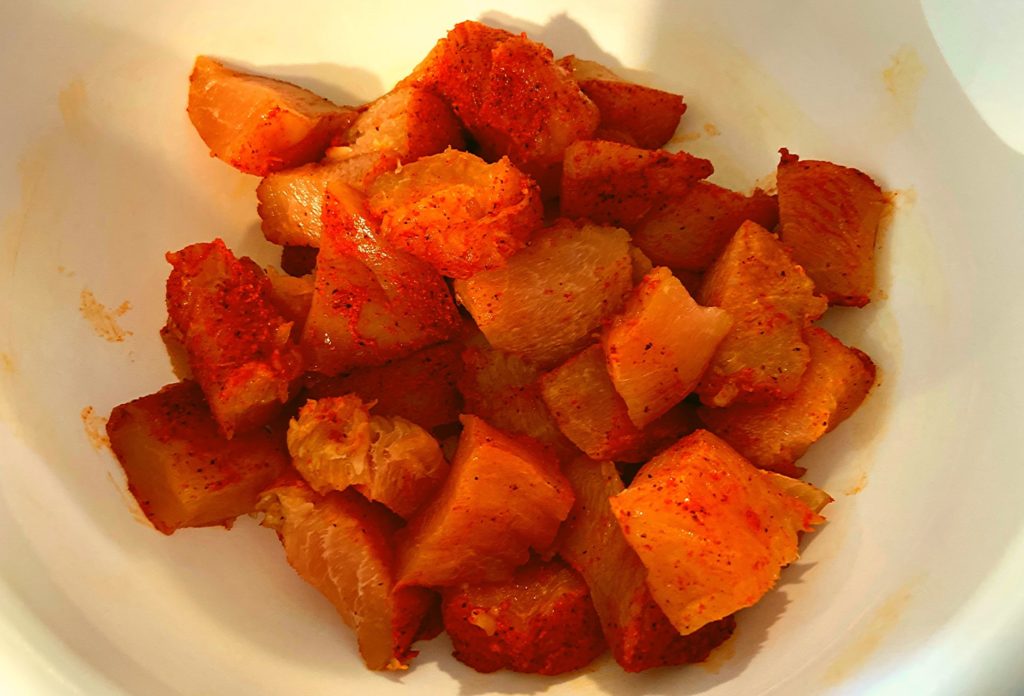 Raw chicken breast cut into bite size pieces in a white bowl with some cajun seasoning.