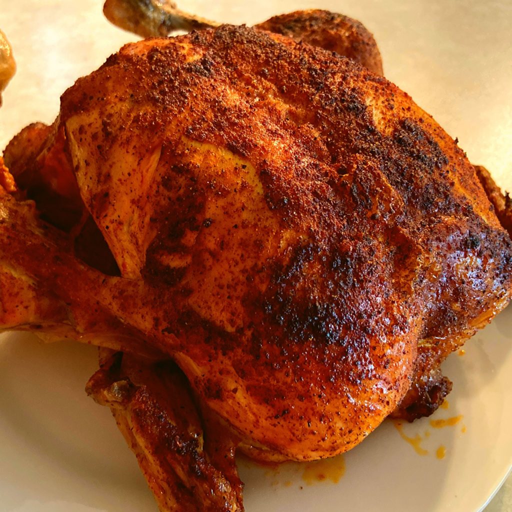 A whole chicken with crispy browned skin sitting on a white plate on a kitchen counter.