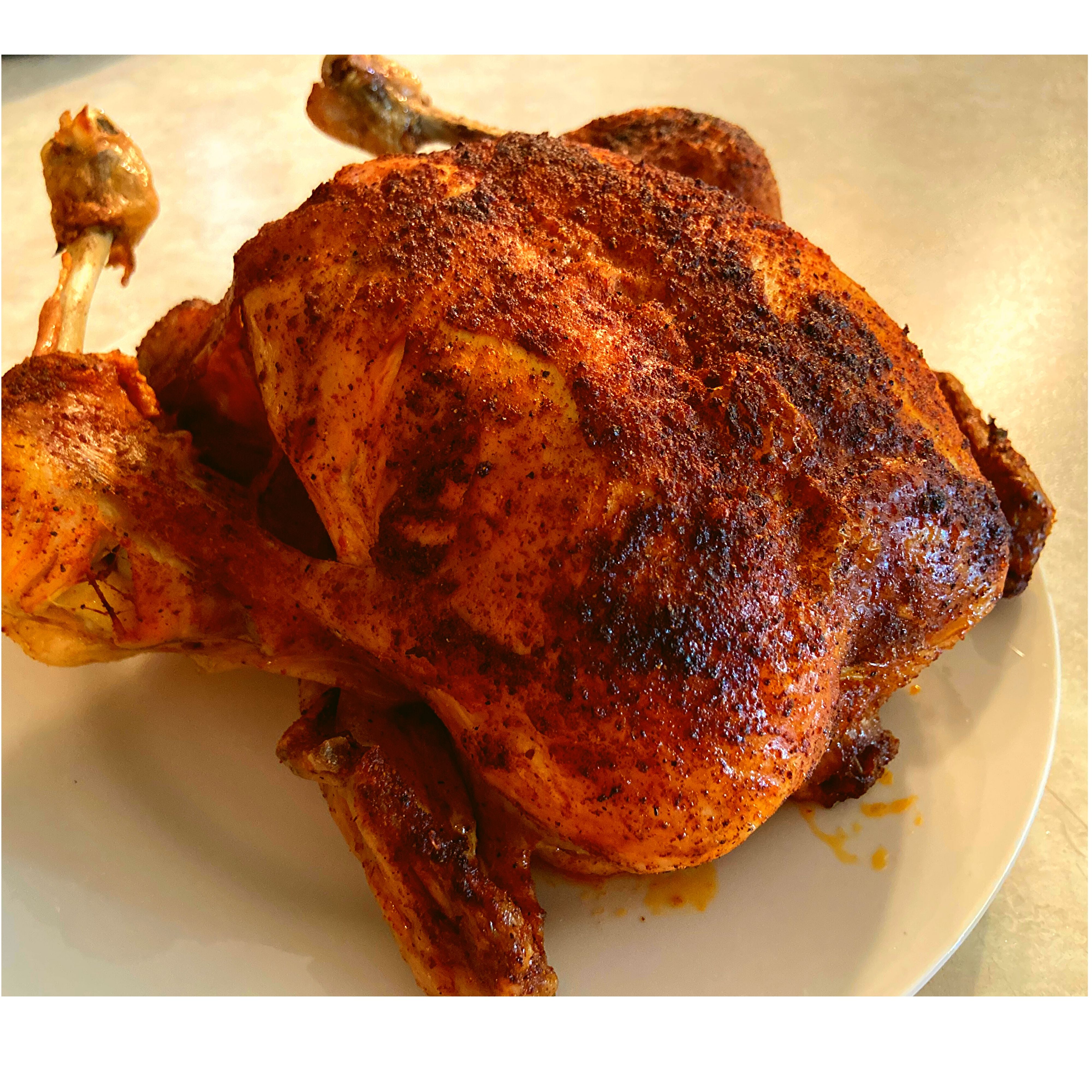 A whole chicken with crispy browned skin sitting on a white plate on a kitchen counter.