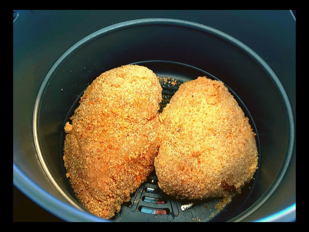 The inside of a Instant Pot Duo Crisp plus air fryer with two raw breaded chicken breasts sitting in the air fryer basket.