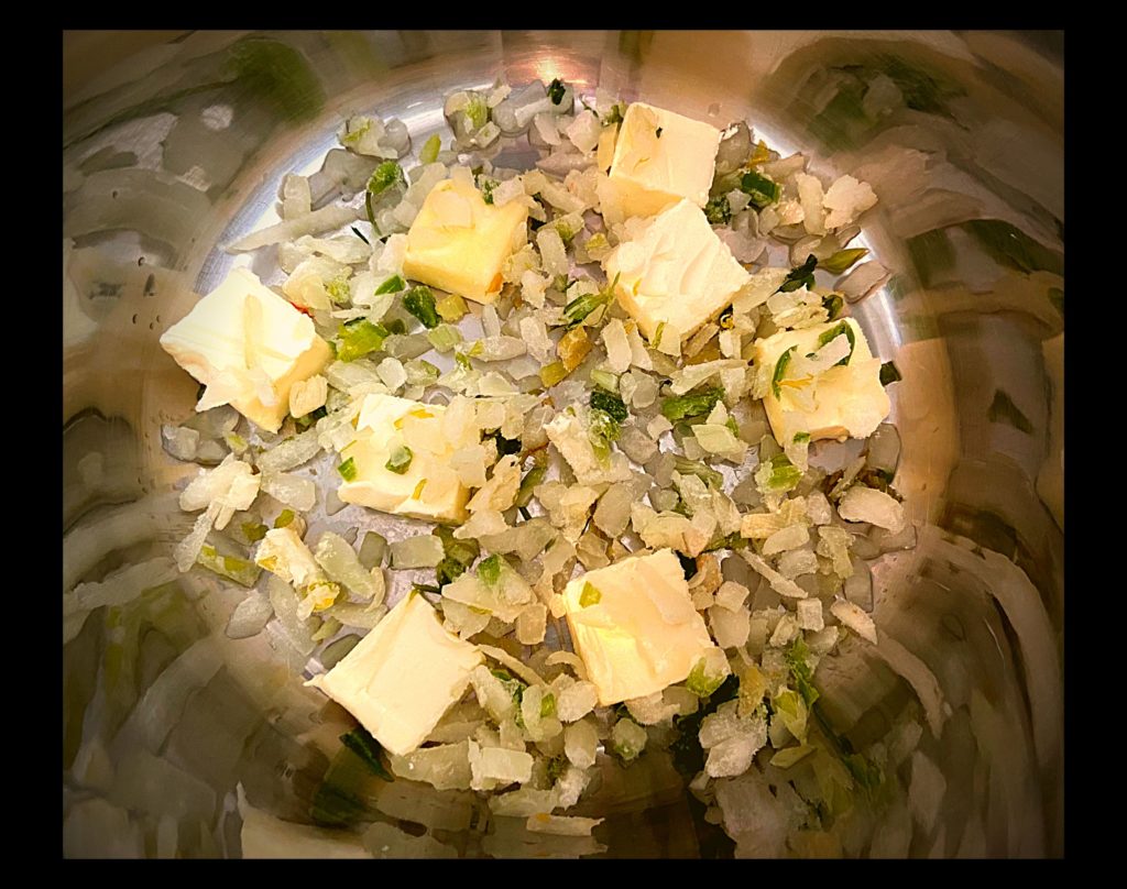 The inside of an Instant Pot filled with diced onions & bell peppers and a sliced stick of butter