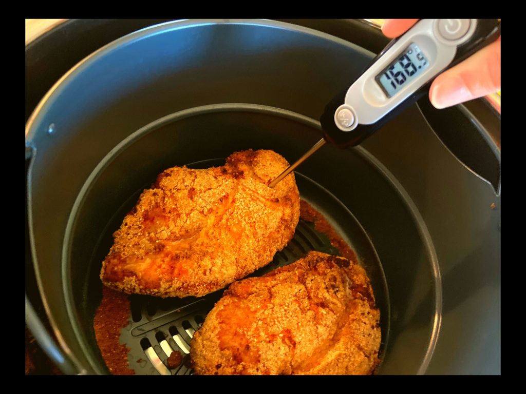 Two breaded cooked chicken breasts sitting in an Instant Pot Duo Crisp Air Fryer with a meat thermometer taht reads 168 degrees.