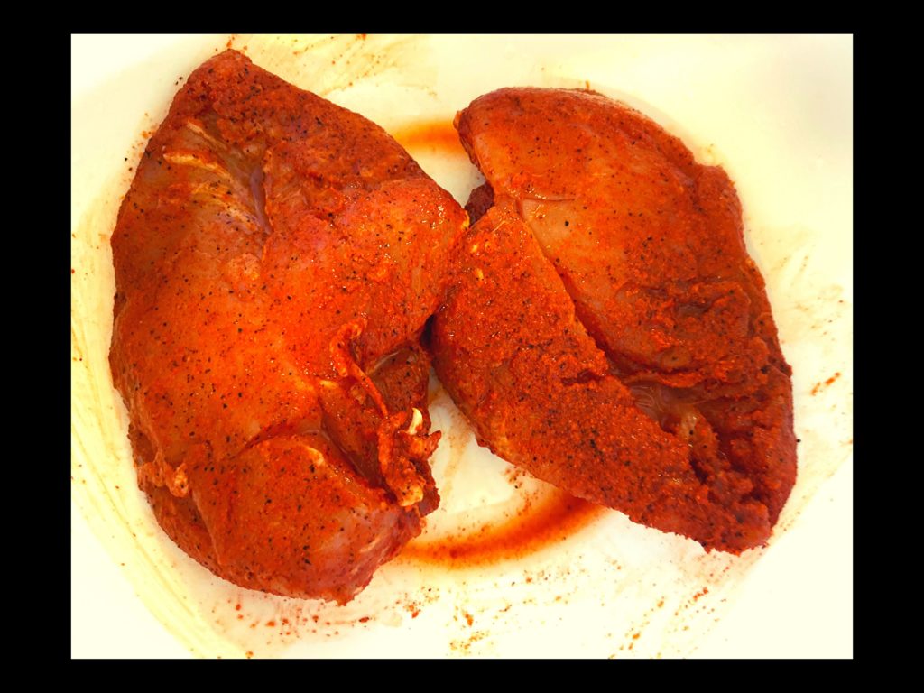 Two raw chicken breasts covered in cajun seasoning in a white bowl.