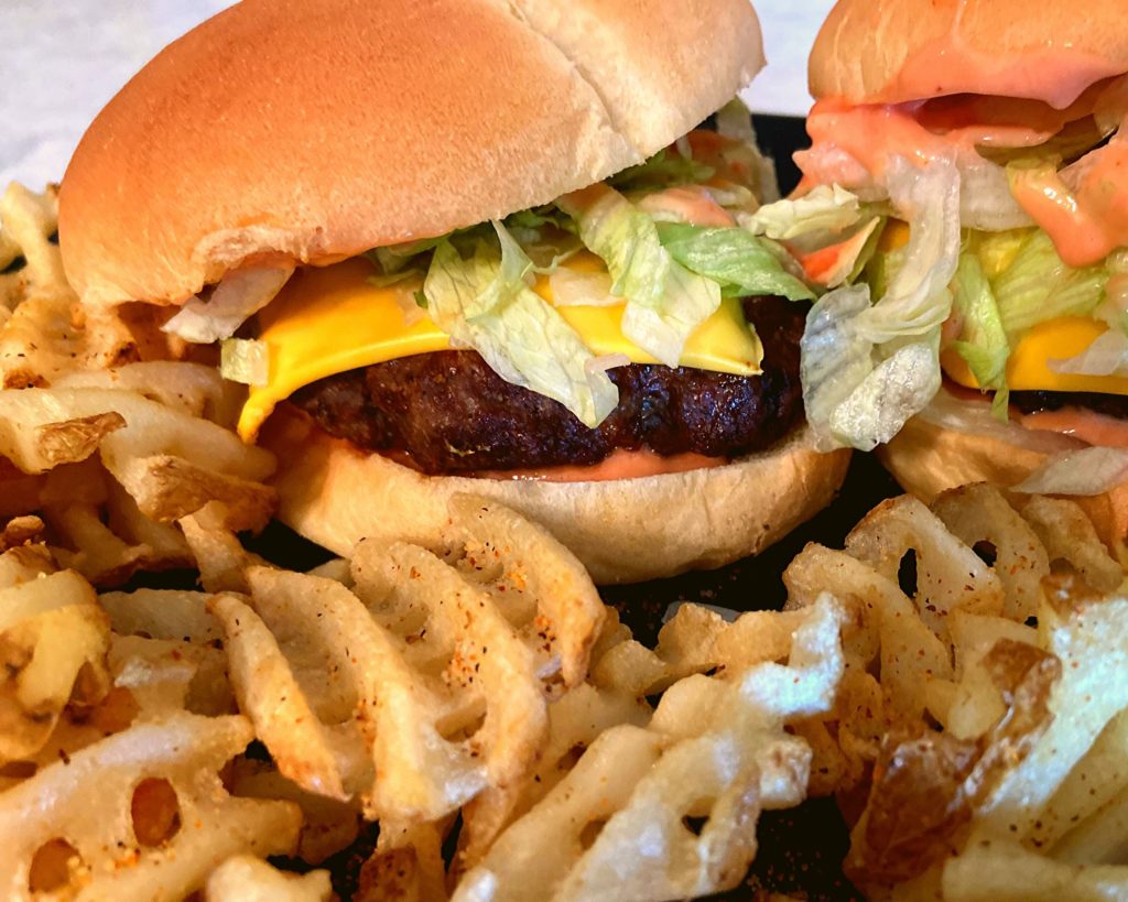 Two Instant Pot Duo Crisp Cheesburgers on a black plate next to some waffle fries.