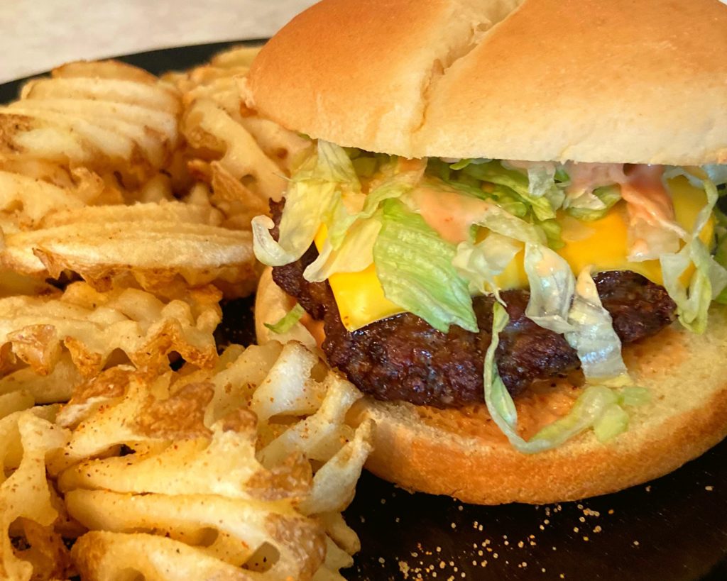 A Instant Pot burger sitting on a black plate next to some waffle fries.