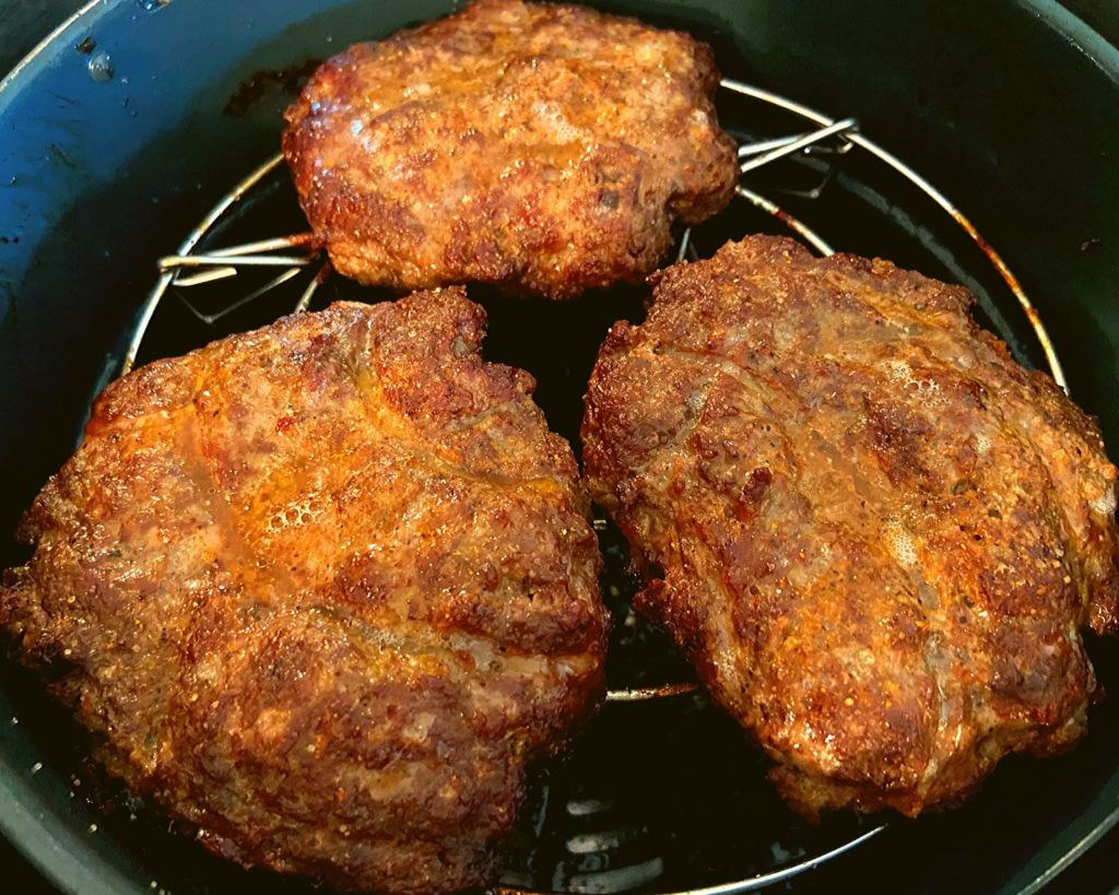 3 partially cooked hamburger patties sitting in an Instant Pot Duo Crisp plus Air fryer.