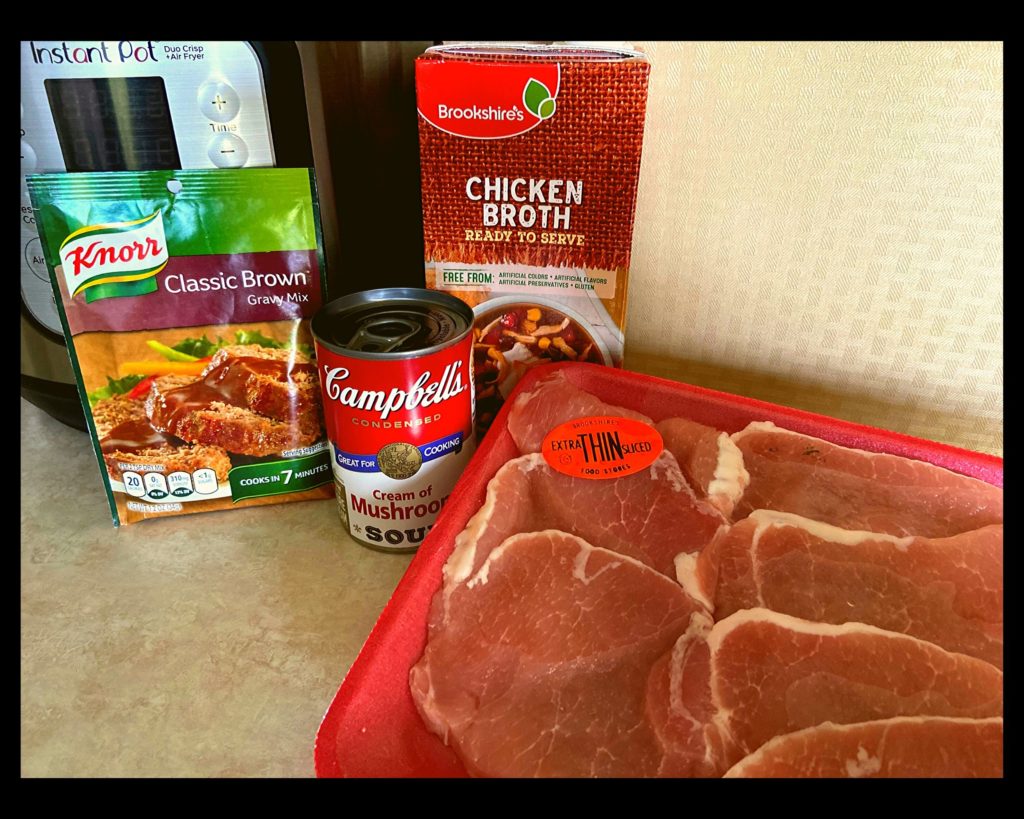 An Instant Pot, container of chicken broth, packet of brown gravy, campbells cream of mushroom soup, and boneless pork chops.