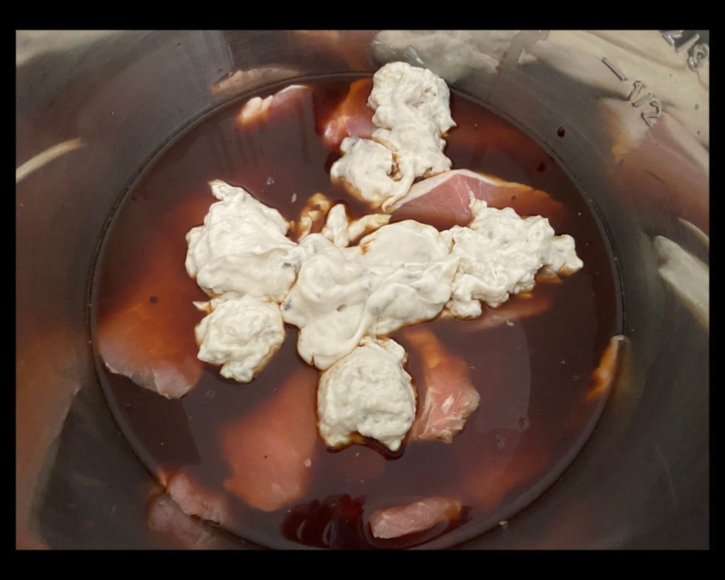 The inside of an Instant pot with brown liquid gravy, boneless pork chops, and cream of mushroom soup on top.