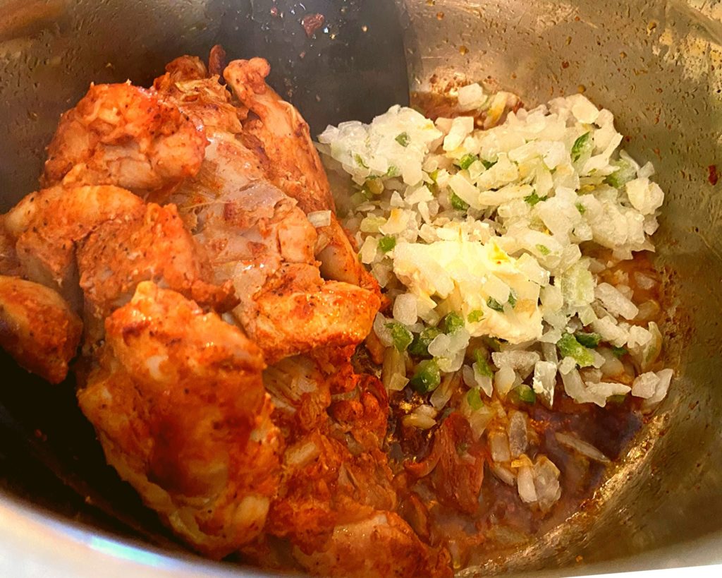 Browned chicken thighs next to uncooked onions and bell peppers in an Instant Pot