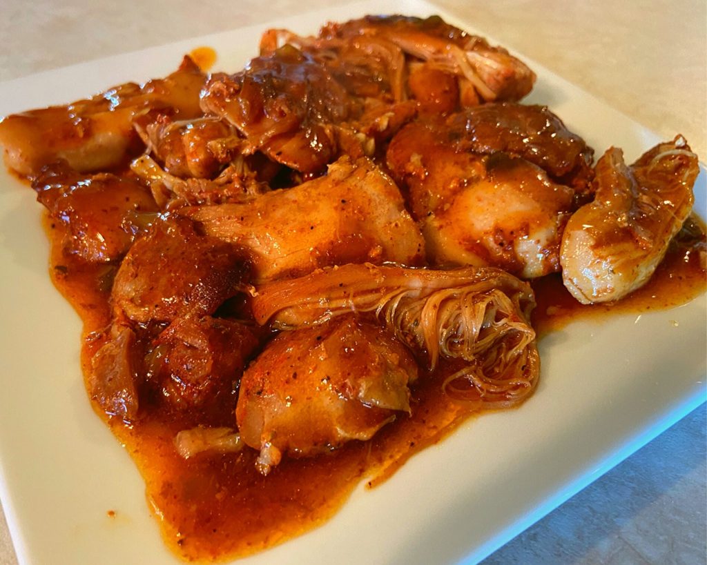 Chicken thighs in a gravy on a square white plate.