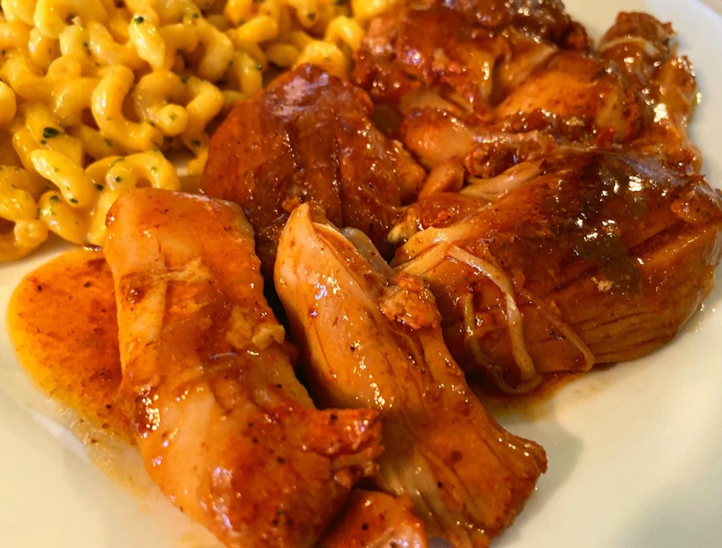 Instant Pot Chicken Thighs in a gravy on a white plate next to spriral macaroni.