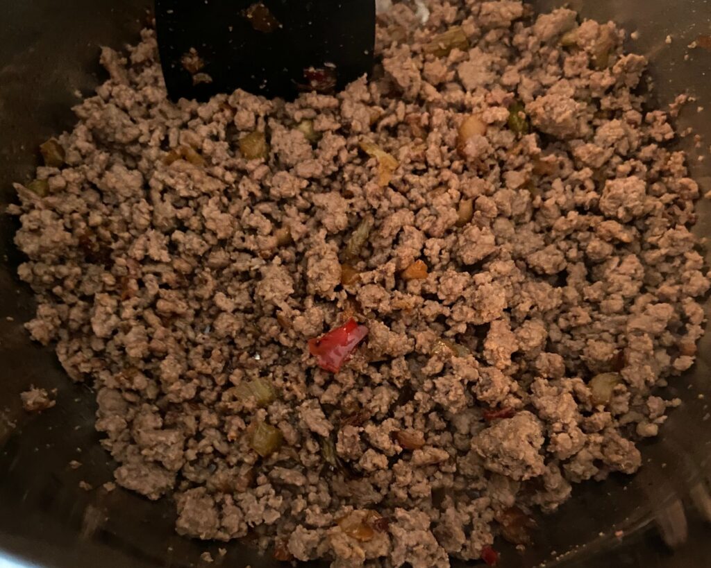 The inside of an Instant Pot with browned ground meat, onion, bell pepper, and celery.