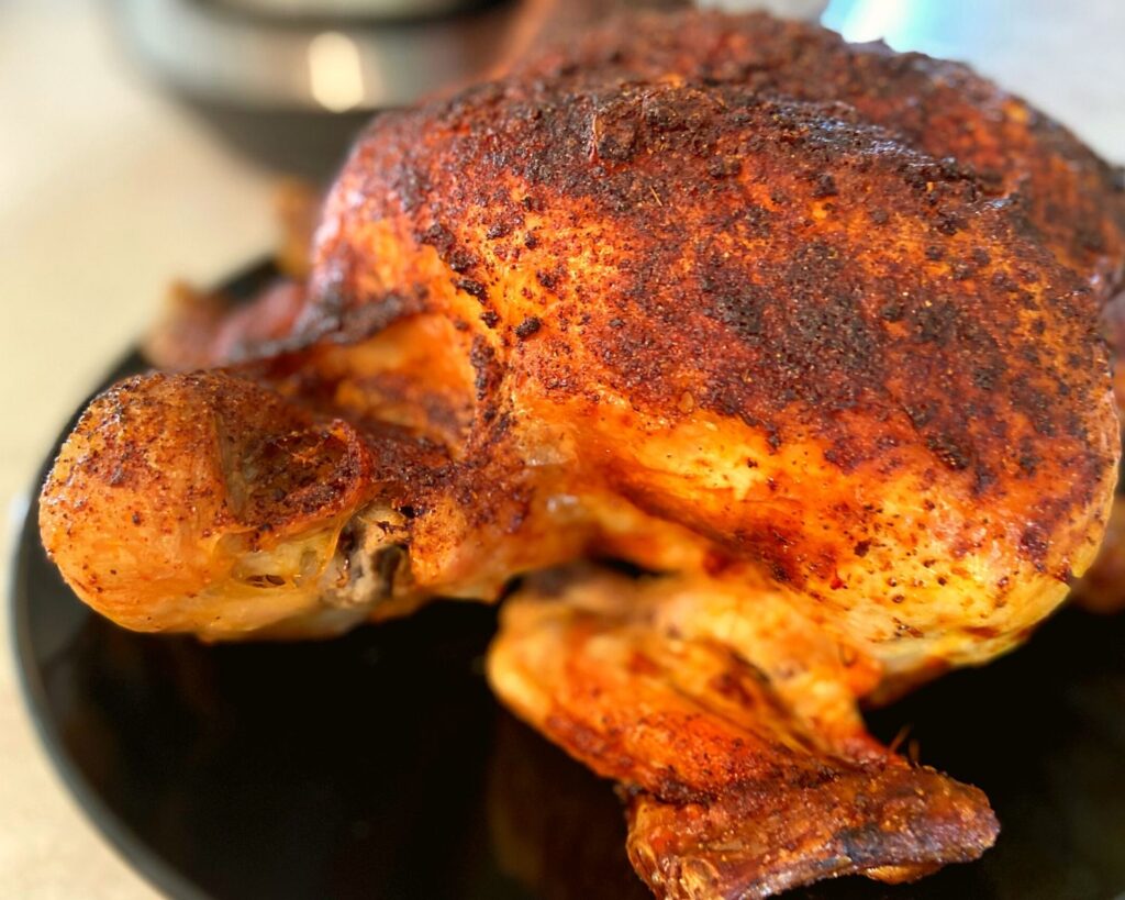 A browned chicken sitting on a black plate in front of an Instant Pot.
