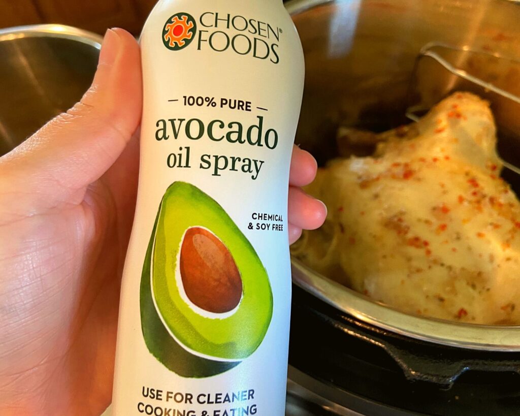 A cooked chicken in an Instant Pot and a spray bottle of avocado oil spray.
