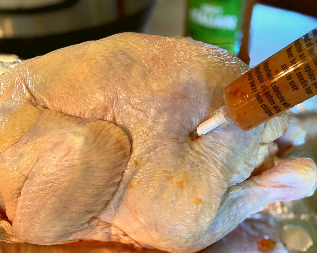 A raw chicken being injected with Italian Dressing.