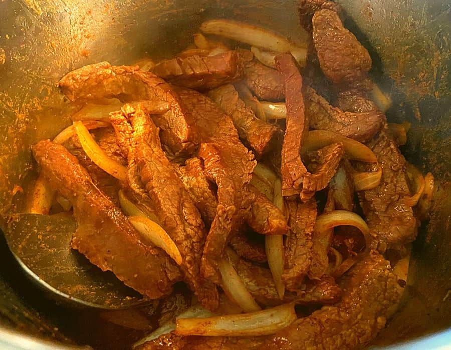 Browned flank steak and onions inside of an Instant Pot