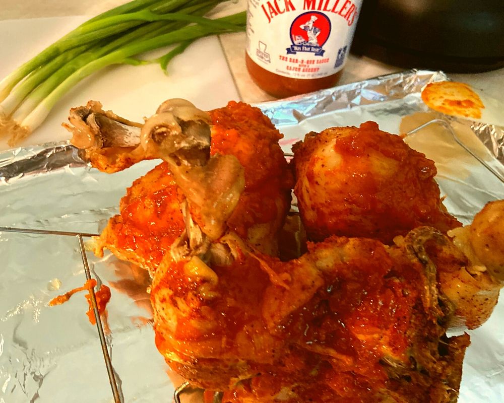 Chicken leg quarters on a tray with bbq sauce being brushed on them.