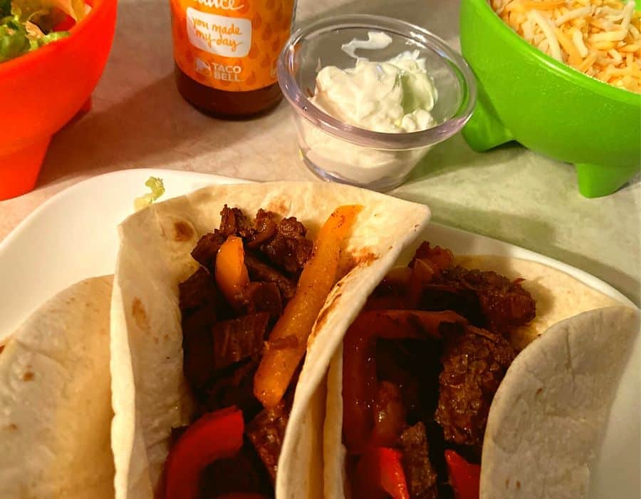 Instant Pot Beef Fajitas on a white plate, next to a green bowl with shredded lettuce and sour cream.