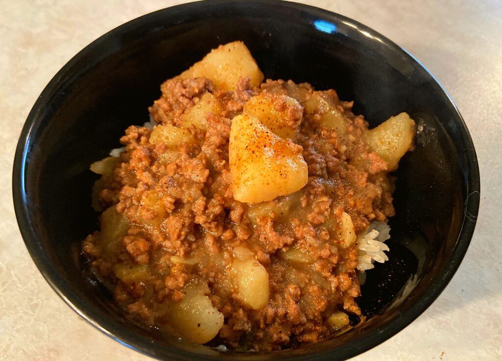 Instant Pot Ground Beef and Potatoes over rice in a black bowl.