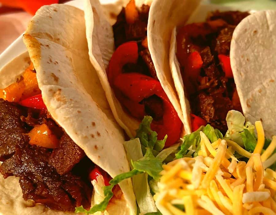 Instant Pot Steak Fajitas on a white plate next to shredded lettucs and cheese.