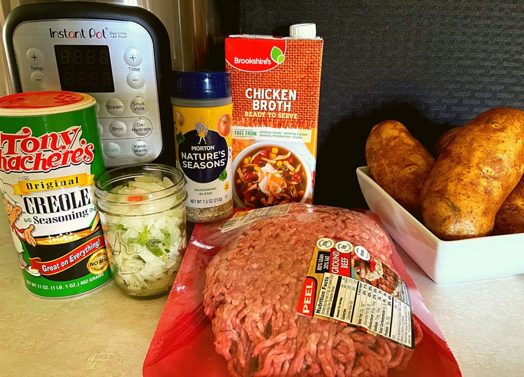 Raw ground meat, tony chachere's, onion, bell pepper, nature seasoning, potatoes, chicken broth, and an Instant Pot on a kitchen counter.