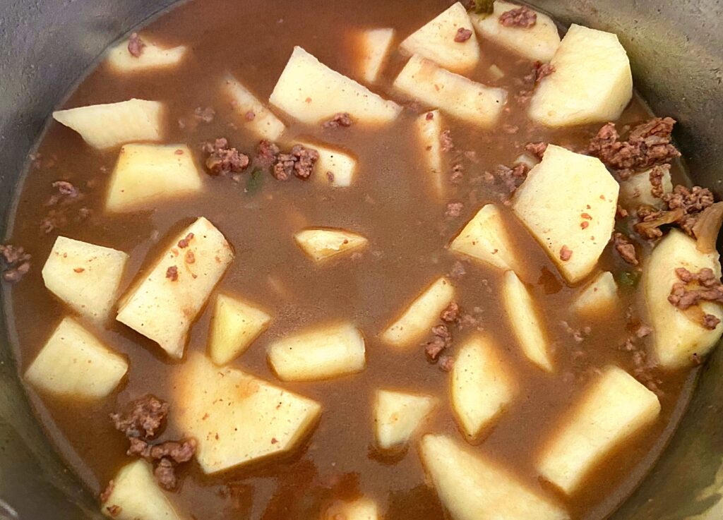 Raw potatoes, ground beef, and gravy inside of an Instant Pot uncooked.