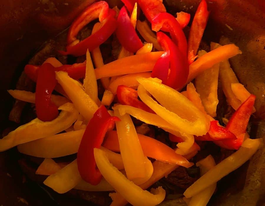 Raw sliced red, orange, and yellow bell peppers inside of an Instant Pot.