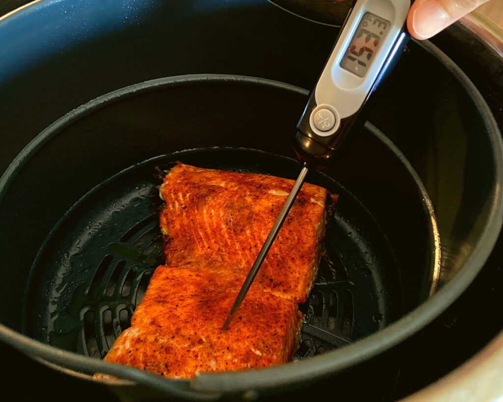 The inside of an Instant Pot Duo Crisp with two cooked salmon fillets and a digitial thermometer reading 153 degrees.