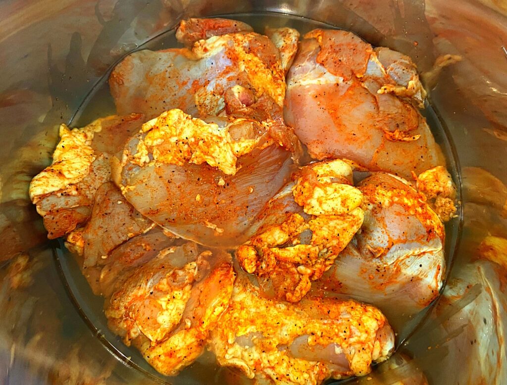 The inside of an Instant Pot filled with marinated chicken thighs and chicken broth.