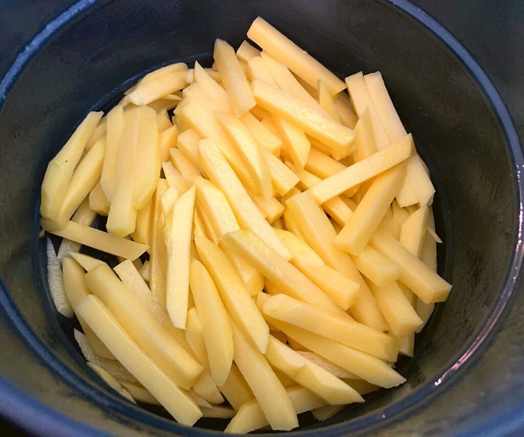 A Instant Pot basket filled with raw french fries.