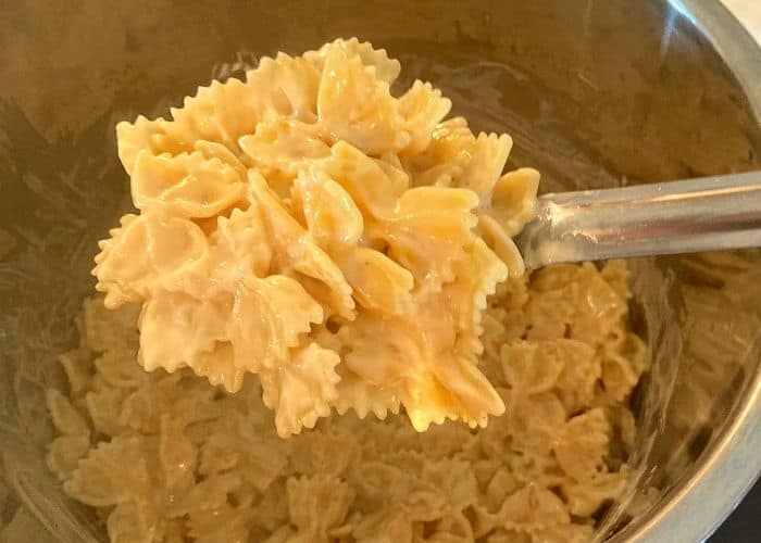 A large spoonfull of cooked bow tie pasta in a white sauce over an Instant Pot filled with bow tie pasta.