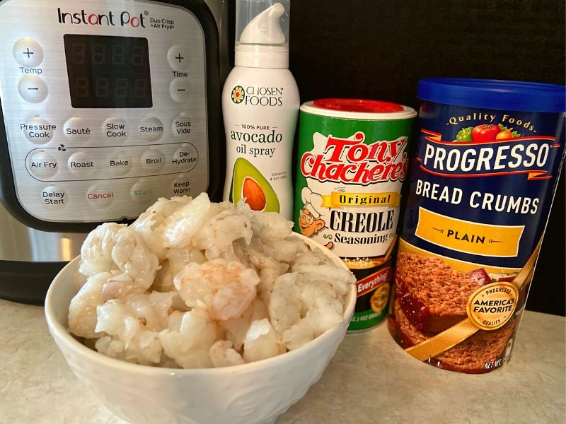 A white bowl of raw shrimp next to an Instant Pot, Avocado Spray, Tony Chachere's Seasoning and Bread Crumbs.