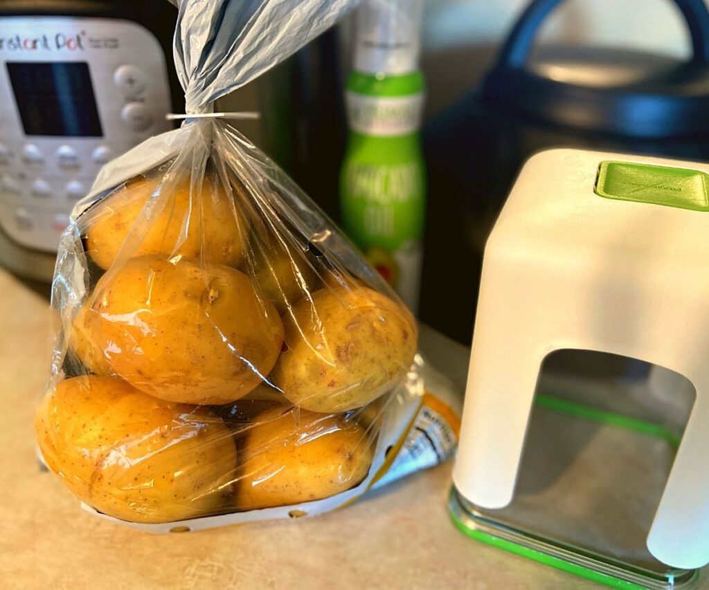 A Instant Pot Duo Crisp, bag of potatoes, Avocado Oil Spray,and French Fry Cutter all sitting on a kitchen counter top.