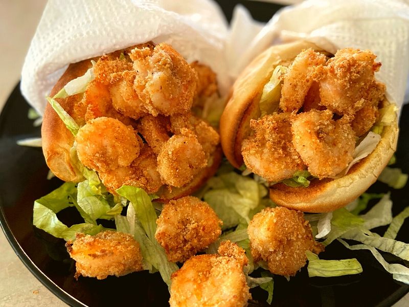 Instant Pot Duo Crisp Air Fryer Fried shrimp in poboy buns with shredded lettuce on a black plate.