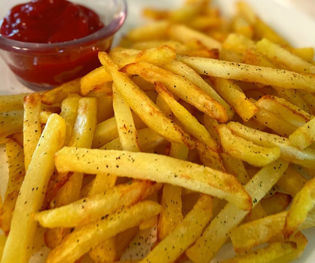 A white plate with french fries and a cup of ketchup.