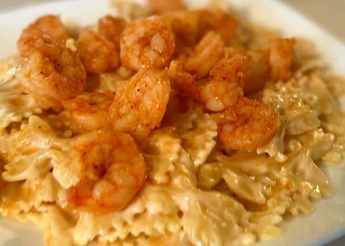 bowtie pasta in a white sauce covered with shrimp on a white square plate