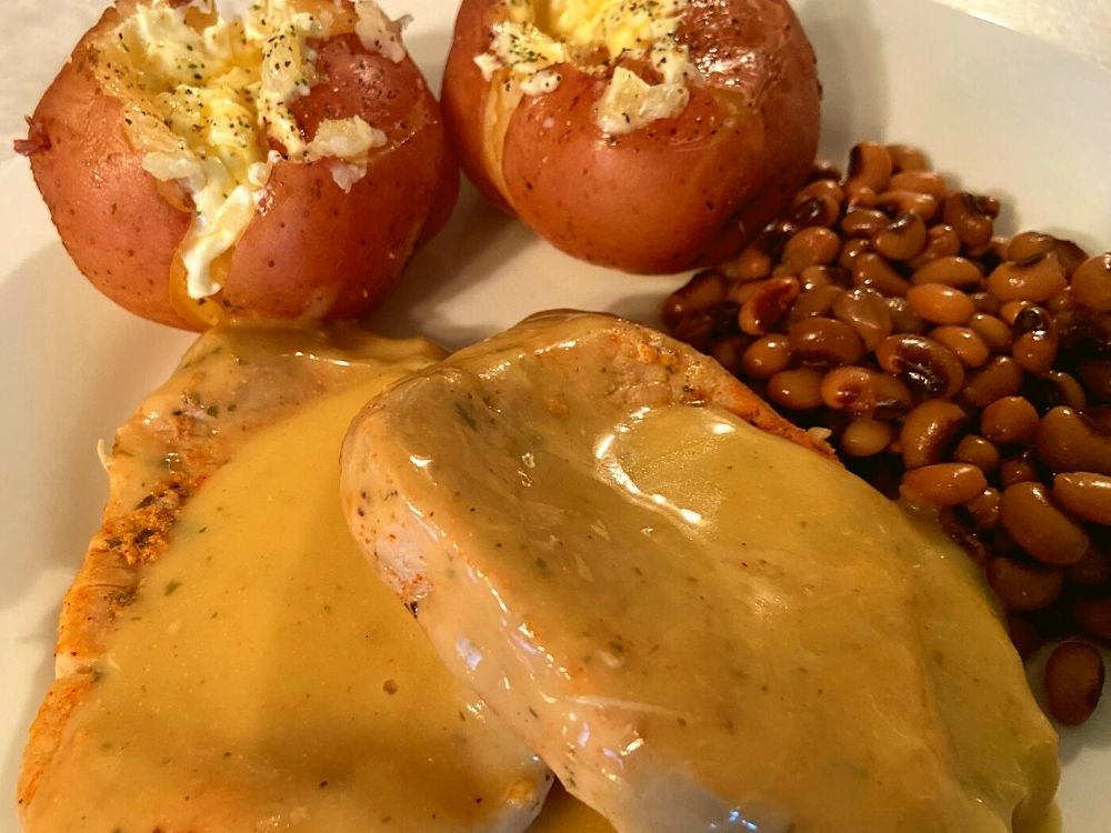 A white plate with instant pot ranch pork chops, red potatoes, and black eye peas on a counter.